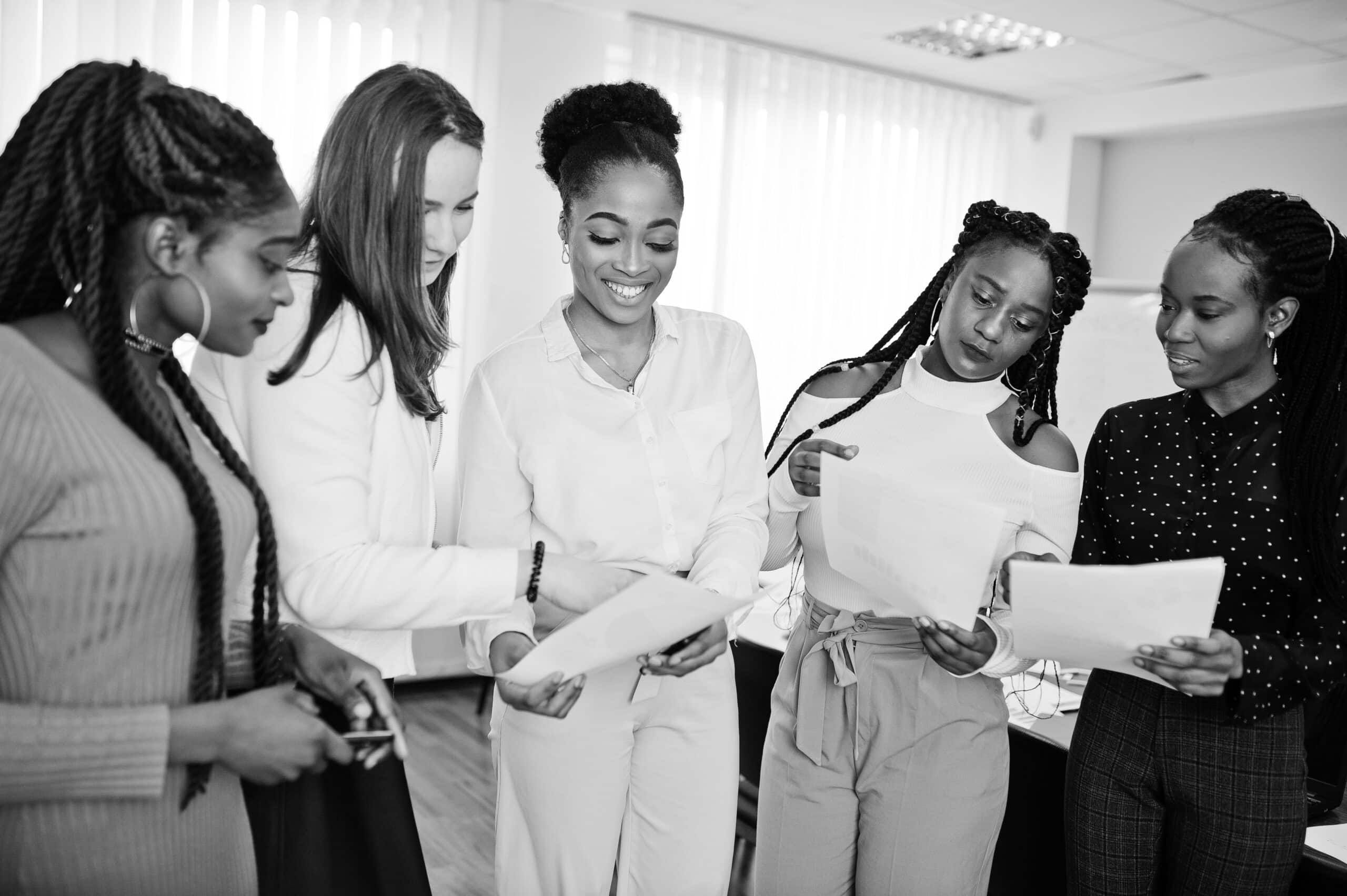 Five multiracial business womans standing at office with papers on hands. Diverse group of female employees in formal wear.
